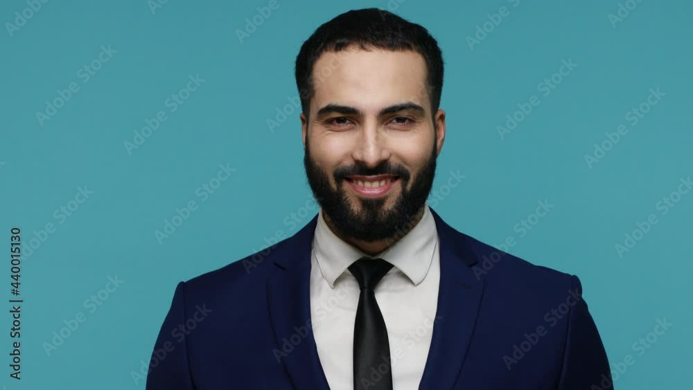 Handsome brutal man looking smiling at camera, winking his eye, flirting with girl, having positive emotions, expressing optimism. Indoor studio shot isolated on blue background. Handsome brutal man looking smiling at camera, winking his eye, flirting with girl, having positive emotions, expressing optimism. Indoor studio shot isolated on blue background.