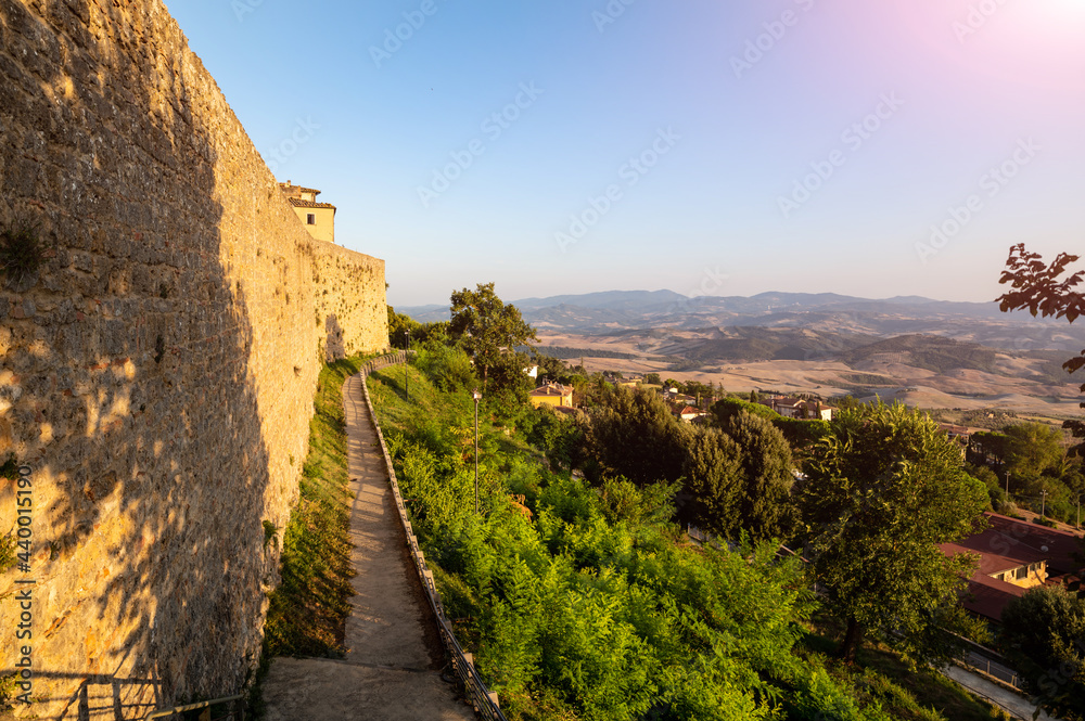 Volterra, Tuscany, Italy. August 2020. The walls of the historic village. The warm light of the late afternoon enhances the massive stone wall, at its foot the perimeter path. Tuscan landscape.