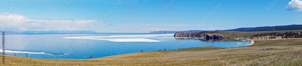 Baikal Lake in May. Panoramic view on the Small Sea Strait with melting ice off the coast and meadows of Olkhon Island with grazing herds. Beautiful landscape. Natural spring background