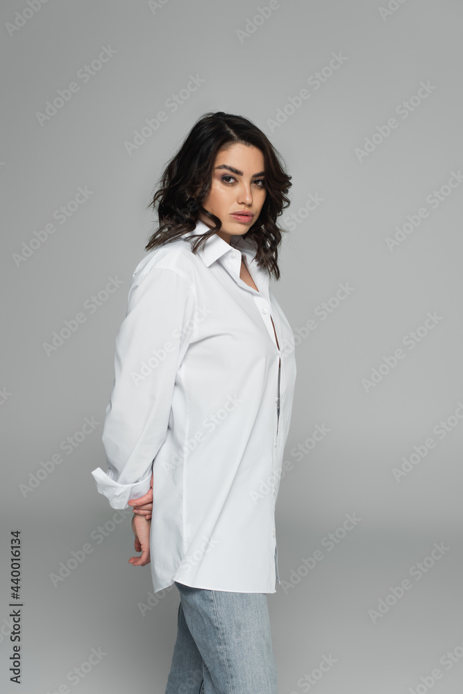 Brunette woman in jeans and shirt standing isolated on grey Brunette woman in jeans and shirt standing isolated on grey