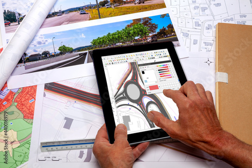 Urbanisme - Aménagement du territoire - employé tenant une tablette numérique au dessus de cartes et plan de masse d'un projet de voirie et giratoire photo