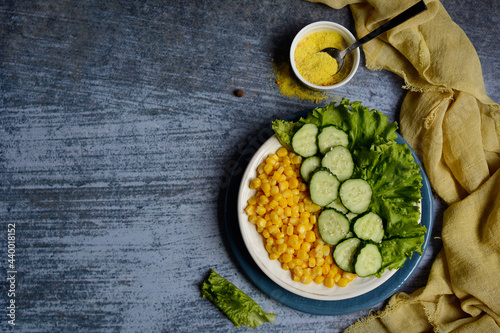 Top view of a plate with corn, cucumbers, lettuce and spices on a blue background. Layout, copy space