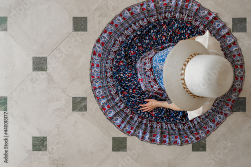 Woman wearing blue dress and white hat sitting on tile floor view from above