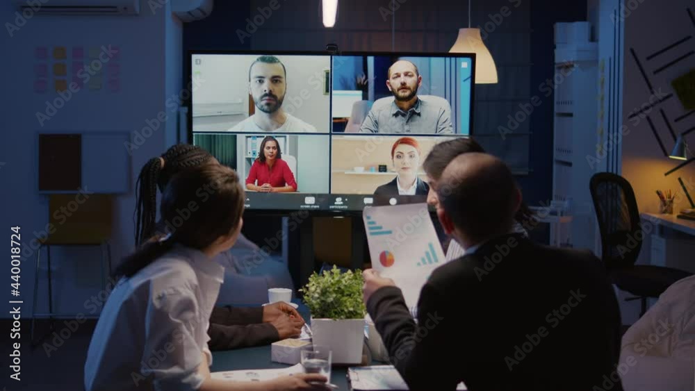 Multi ethnic businesspeople discussing company statistics with remote coworkers during online videocall conference meeting brainstorming ideas. Diverse teamwork working overtime in corporate room