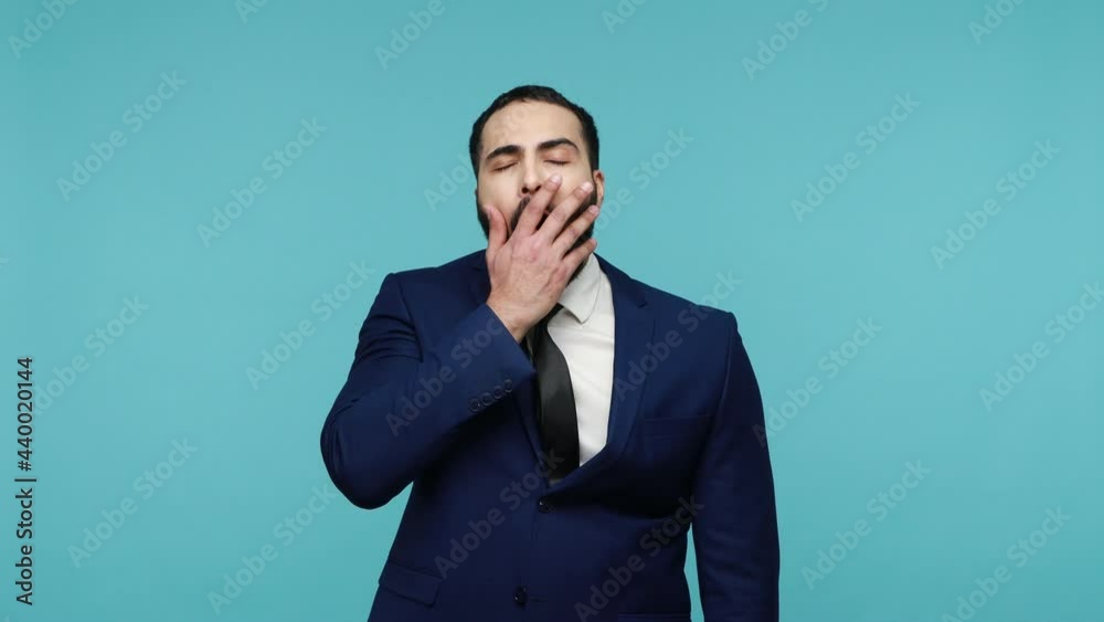 Drowsy tired bearded man in formal suit need rest, yawning wide feeling sleepy exhausted, difficult wake up, having insomnia chronic fatigue syndrome. Indoor studio shot isolated on blue background. Drowsy tired bearded man in formal suit need rest, yawning wide feeling sleepy exhausted, difficult wake up, having insomnia chronic fatigue syndrome. Indoor studio shot isolated on blue background.