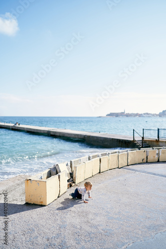 Kid crawls along the beach near the breakwater against the background of the sea