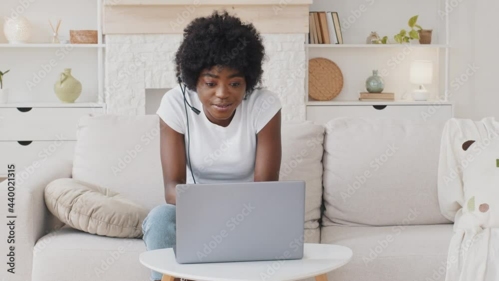Happy African American young woman wear headset communicating by conference call speak looking at laptop at home, video chat by webcam distance language course class with computer education concept