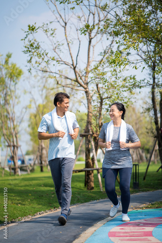Asian mature man and woman running outdoors. Happy mature couple in summer sports running outfit. © Thirawatana