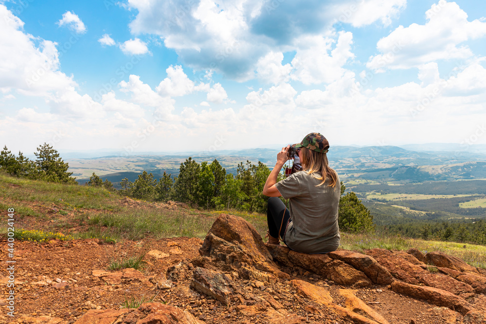 Naklejka premium Tourist girl photographing with vintage photo camera at the top of the mountain peak
