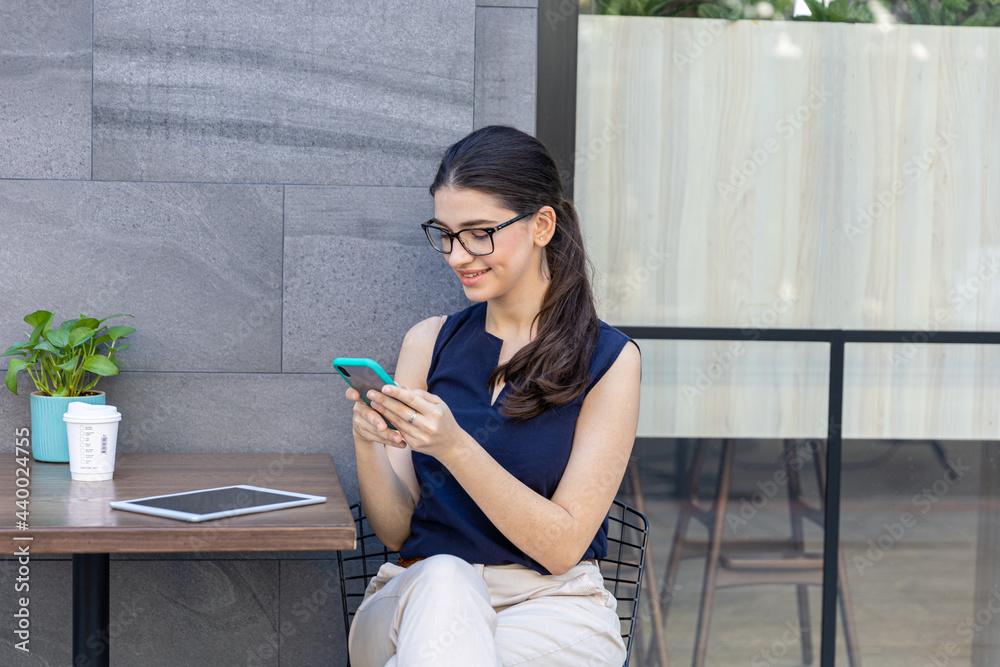 Young attractive girl holding  a smart phone checking or making social connection at an outdoor café on the street. Woman in casual using technology while having tea or coffee outside