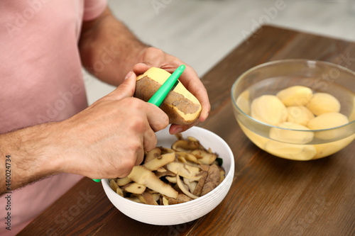 Man peeling potato at table, closeup. Preparing vegetable