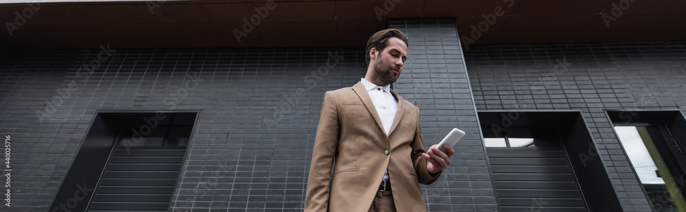 low angle view of young businessman in formal wear using smartphone outside, banner. low angle view of young businessman in formal wear using smartphone outside, banner.