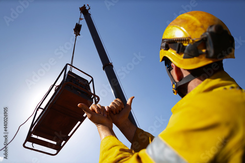 Safe work practice rigger wearing fall protection helmets giving crane operator hand signal by holding up two hand against each other pointing boths thump out meant crane boom is giging out slowly     photo