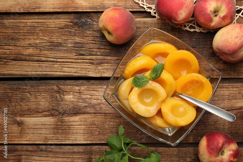 фотографія Canned peach halves in glass bowl on wooden table, flat lay