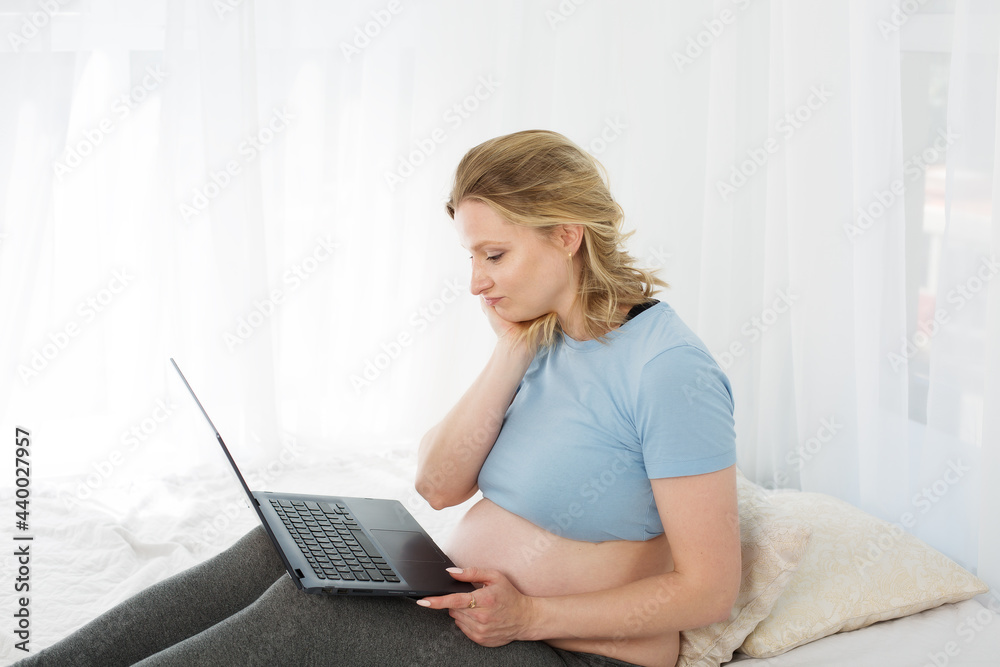 Blonde pregnant woman working on a computer on the bed, online shopping Blonde pregnant woman working on a computer on the bed, online shopping