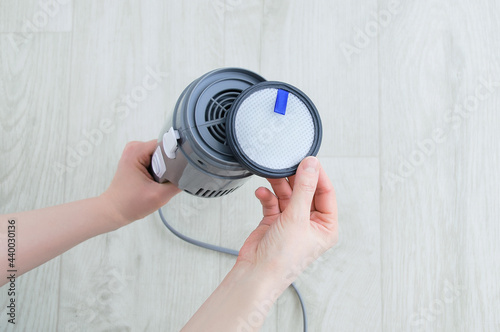 Close-up of putting the filter on vacuum cleaner. White wood floor.