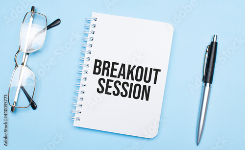 breakout session words in white notepad, pen and glasses on blue background. Concept