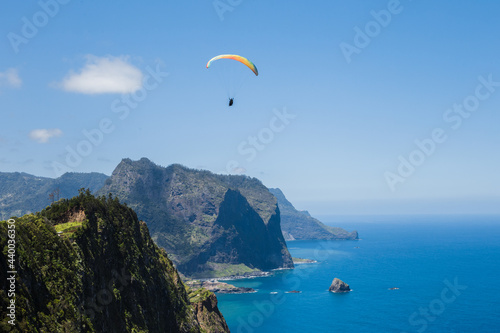 Overview of paraglider flying over Porto da Cruz village with Penha D'aguia mountain as background in Madeira island.