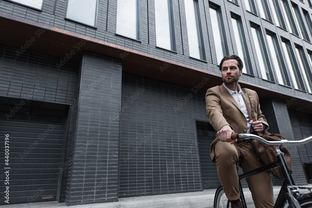 young businessman in suit with leather bag riding bicycle outside.