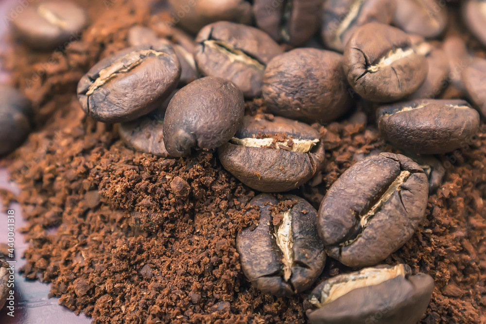 Roasted coffee beans lie on top of a pile of ground coffee