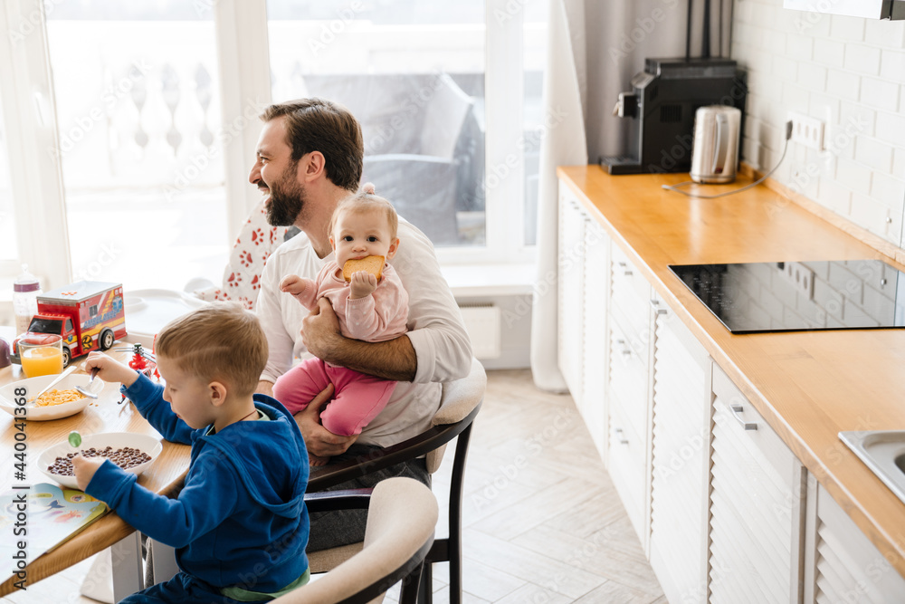 White father smiling while having breakfast with his children at home White father smiling while having breakfast with his children at home