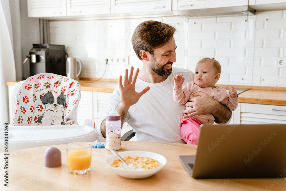 White father gesturing and holding his daughter while using laptop White father gesturing and holding his daughter while using laptop