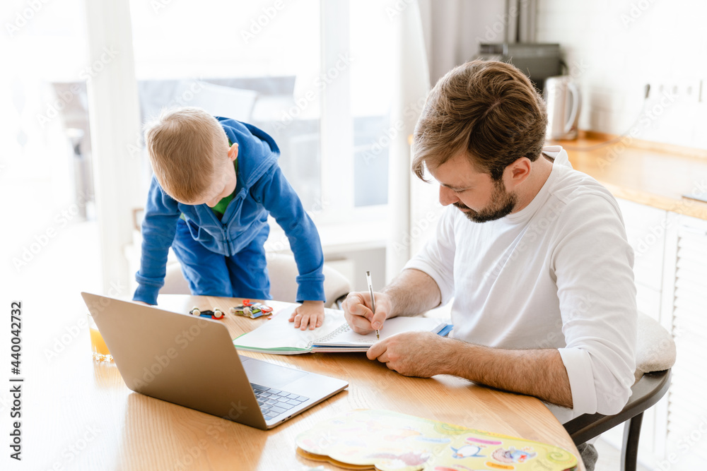 White father and son drawing and using laptop in kitchen at home White father and son drawing and using laptop in kitchen at home