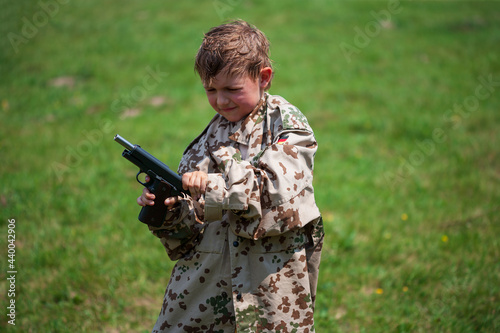 Boy in military uniform with weapon learns to shoot outdoors