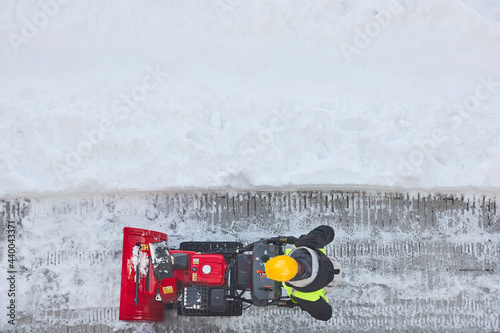 Worker cleaning snow on the sidewalk with a snowblower. Wintertime photo