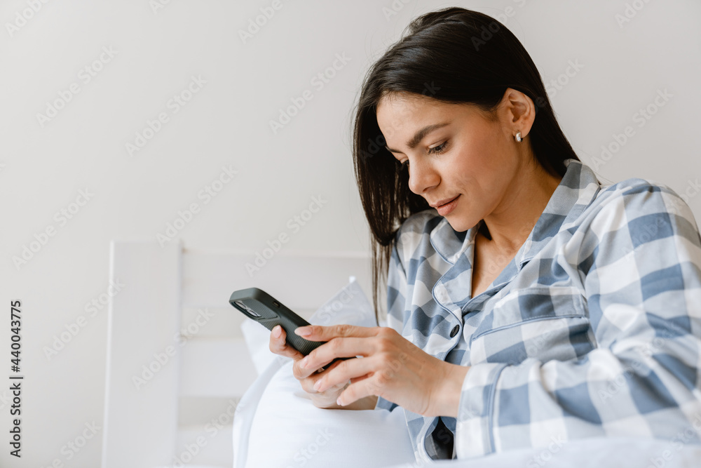 Young hispanic woman using cellphone while lying in bed at home Young hispanic woman using cellphone while lying in bed at home