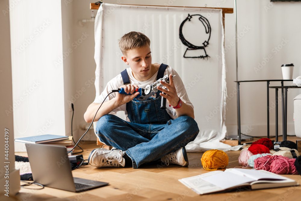 Young white man using laptop and sewing machine
