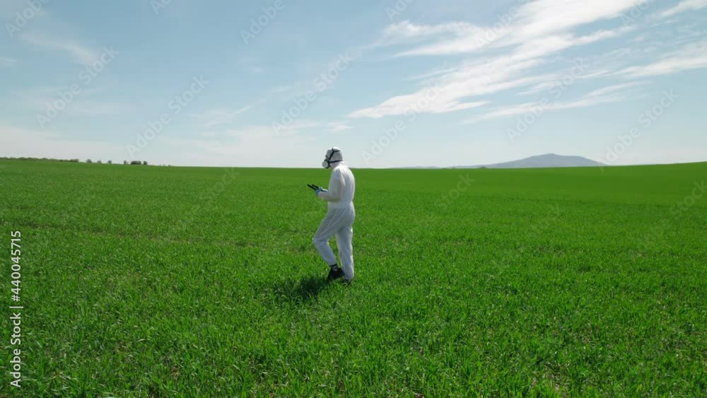 Scientist biologist in a gas mask and protective suit examines the field with the help of modern technologies.The camera moves slightly, in the background you can see the grain to the horizon and hill Scientist biologist in a gas mask and protective suit examines the field with the help of modern technologies.The camera moves slightly, in the background you can see the grain to the horizon and hill