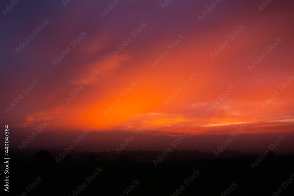 rich orange sunset with the sun behind the clouds and a line of trees in the background