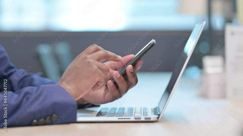 Close up of Hands of African Businessman with Laptop using Smartphone Close up of Hands of African Businessman with Laptop using Smartphone