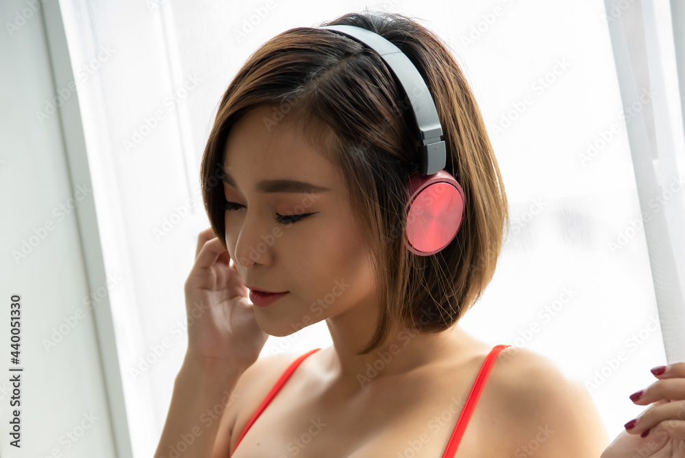 Naklejka premium Beautiful sexy asian woman in red bikini listening to music by the headphone for relaxing at the bedroom.