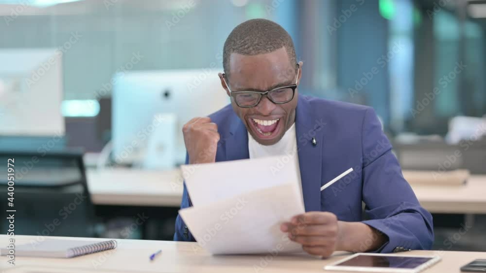 African Businessman Celebrating Success While Reading Documents African Businessman Celebrating Success While Reading Documents