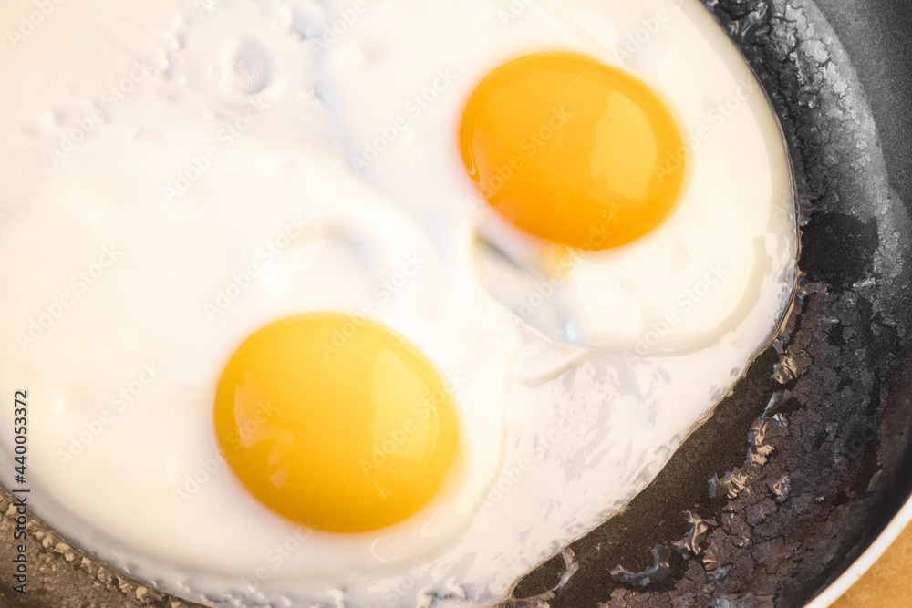 Two bright round raw yolks in whites with edge cracks in a frying pan. Cooked tender, soft fried eggs is a simple dish. Top view Two bright round raw yolks in whites with edge cracks in a frying pan. Cooked tender, soft fried eggs is a simple dish. Top view