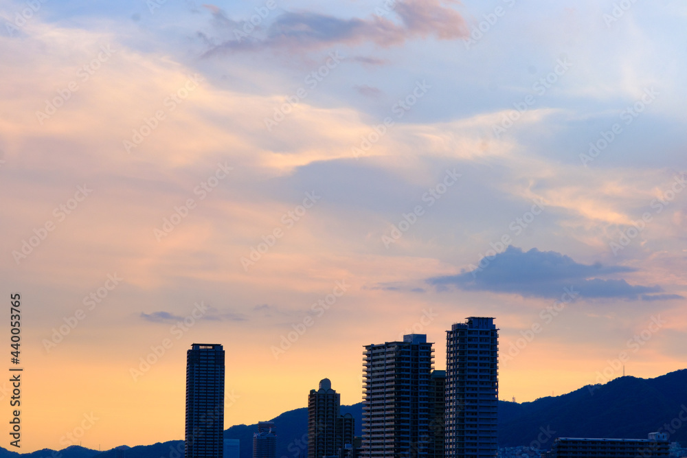 タイトル : 日の入り前の六甲山。西の空と雲がオレンジ色に染まるマジックアワー。高層ビルがシルエットで浮かぶ。１日の終わり。