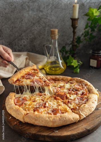 selective focus. hot pizza with cheese and pepperoni. the girl pulls a slice of pizza with melted cheese stretching. vertical position, dark mood