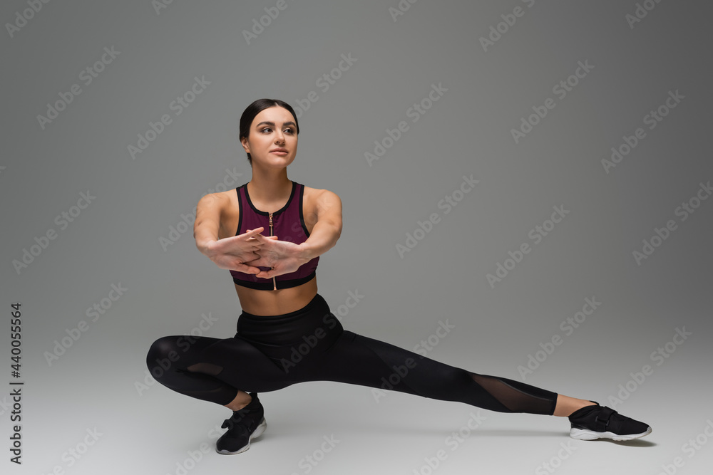 young woman in black sportswear stretching on grey background.