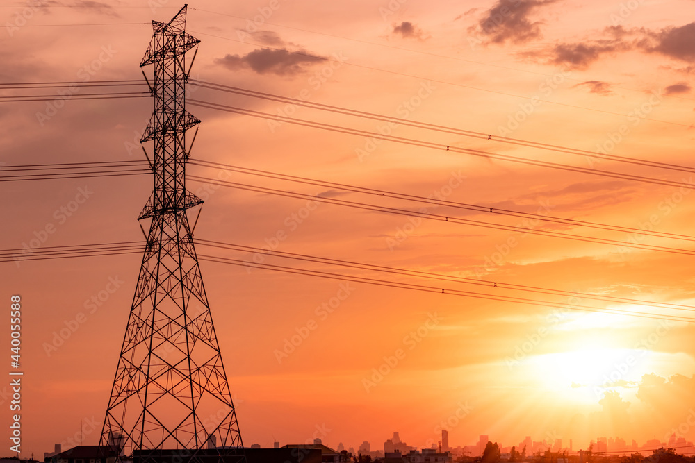 High voltage electric pylon and transmission lines with sunset sky and cityscape. Electricity pylons. High voltage grid tower. High-voltage pole for distribution of electricity to urban communities.