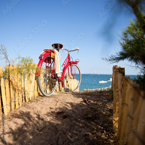 Fototapeta Naklejka Na Ścianę i Meble -  Vieux vélo rouge au soleil en bord de mer, vu sur la plage en été.