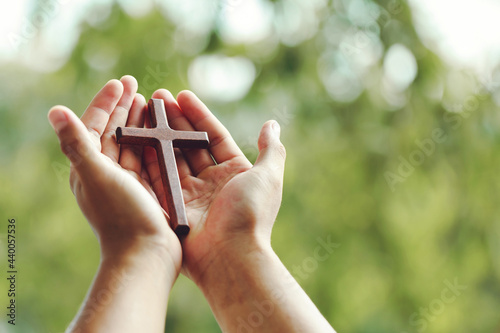 Wooden cross on praying hands with outdoor background. international prayer day.Easter and Good friday concept.