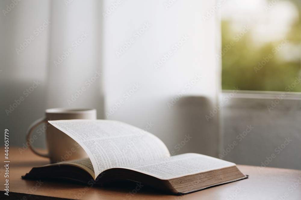 Open bible with a cup of coffee for morning devotion on wooden table with window light.book and coffee cup on wooden table. Open bible with a cup of coffee for morning devotion on wooden table with window light.book and coffee cup on wooden table.