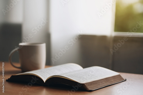Open bible with a cup of coffee for morning devotion on wooden table with window light.book and coffee cup on wooden table.