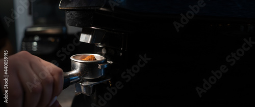 close-up of a barista holding a portafilter with coffee in front of an electric coffee grinder in a cafe. The concept of the process of preparing beans for making morning espresso 
