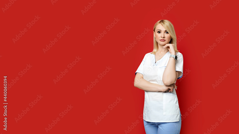 Confident female doctor standing on red background. Young woman intern in medical clothes posing.