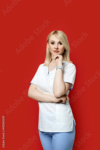 Obraz na płótnie Confident female doctor standing on red background. Young woman intern in medical clothes posing. w salonie