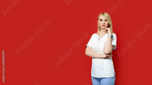 Obraz na płótnie Confident female doctor standing on red background. Young woman intern in medical clothes posing. w salonie
