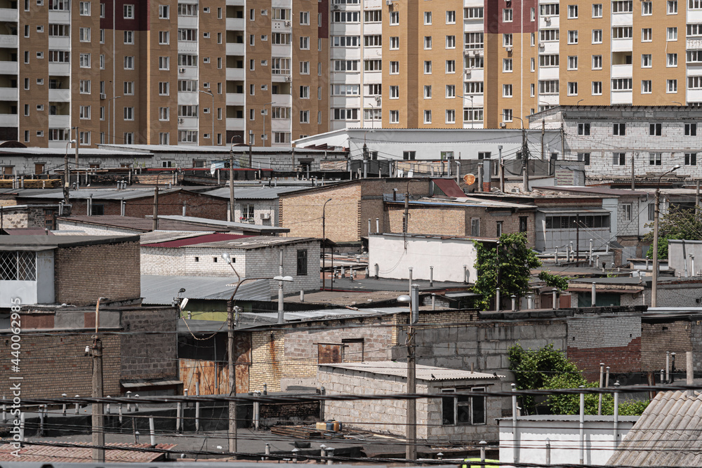 Chaotically densely built-up barracks on the background of multi-storey residential buildings. Kyiv, Ukraine - June 2021.